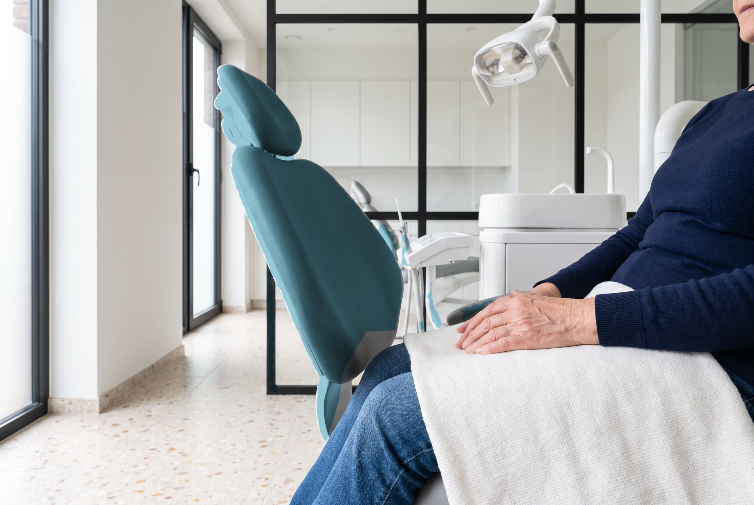An older patient sits calmly in the dental chair with a soft blanket over their lap in a bright treatment room.