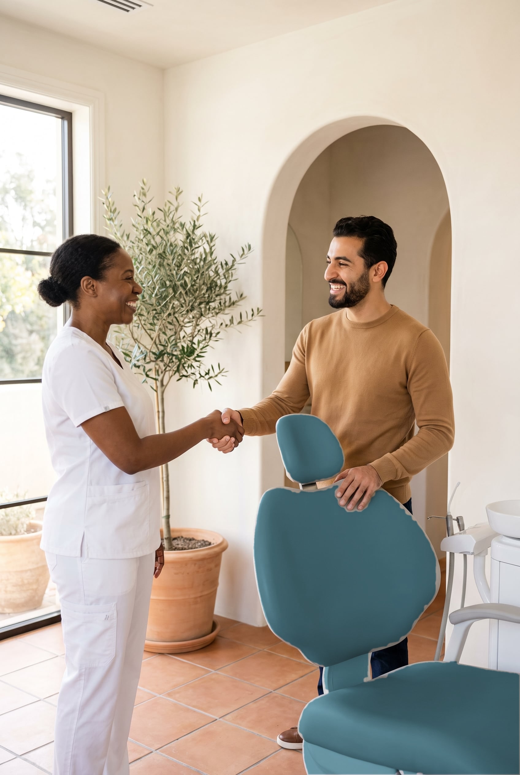A dental assistant in white scrubs shakes hands with a smiling bearded man beside the dental chair.